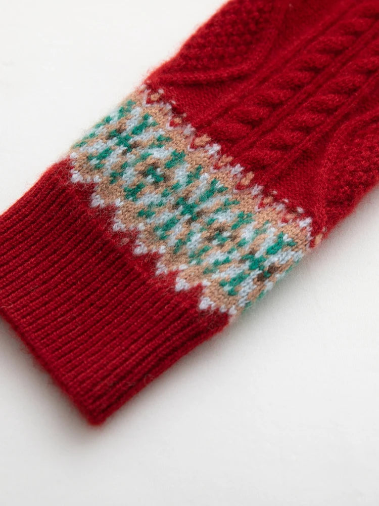 A close-up of a red knit sock featuring a Fair Isle pattern band with green, beige, and white details, set against a plain white background.