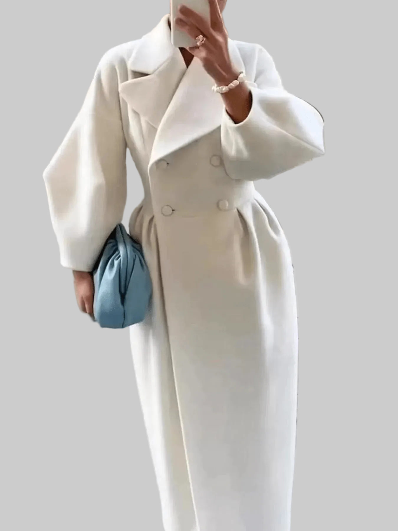 A person wearing a long white double-breasted coat with wide lapels and a gathered waist, holding a light blue clutch bag against a plain beige background.