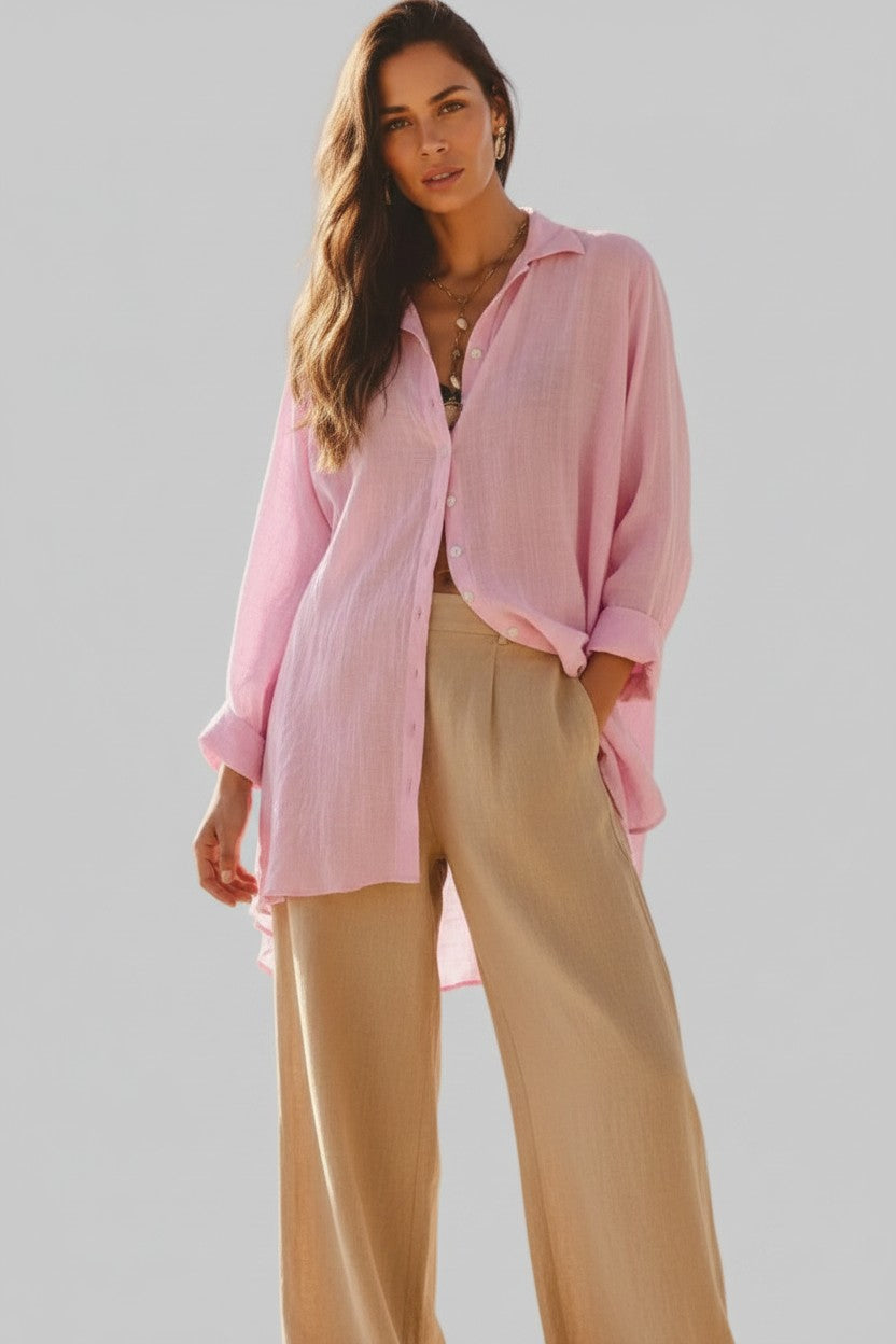 A woman modeling a light pink long-sleeve button-up shirt and beige wide-leg trousers against a solid gray studio background.