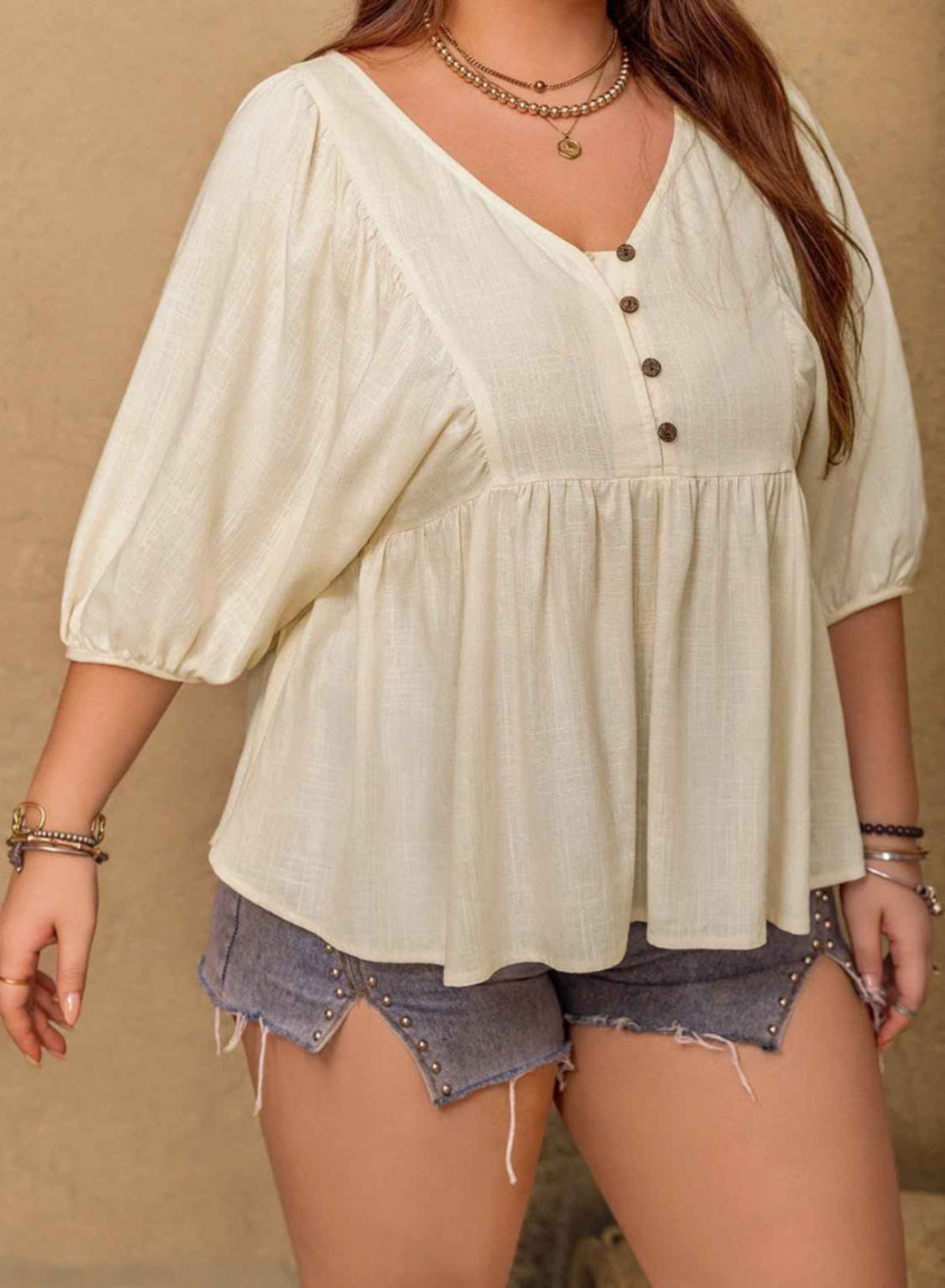 Woman wearing a light-colored blouse with button details and denim shorts on a beige background