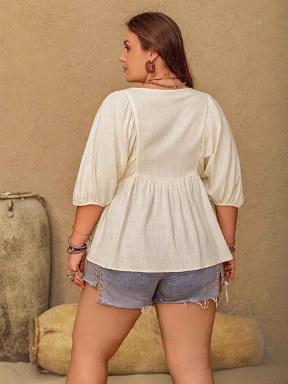 Woman wearing a light-colored blouse and denim shorts against a beige wall.