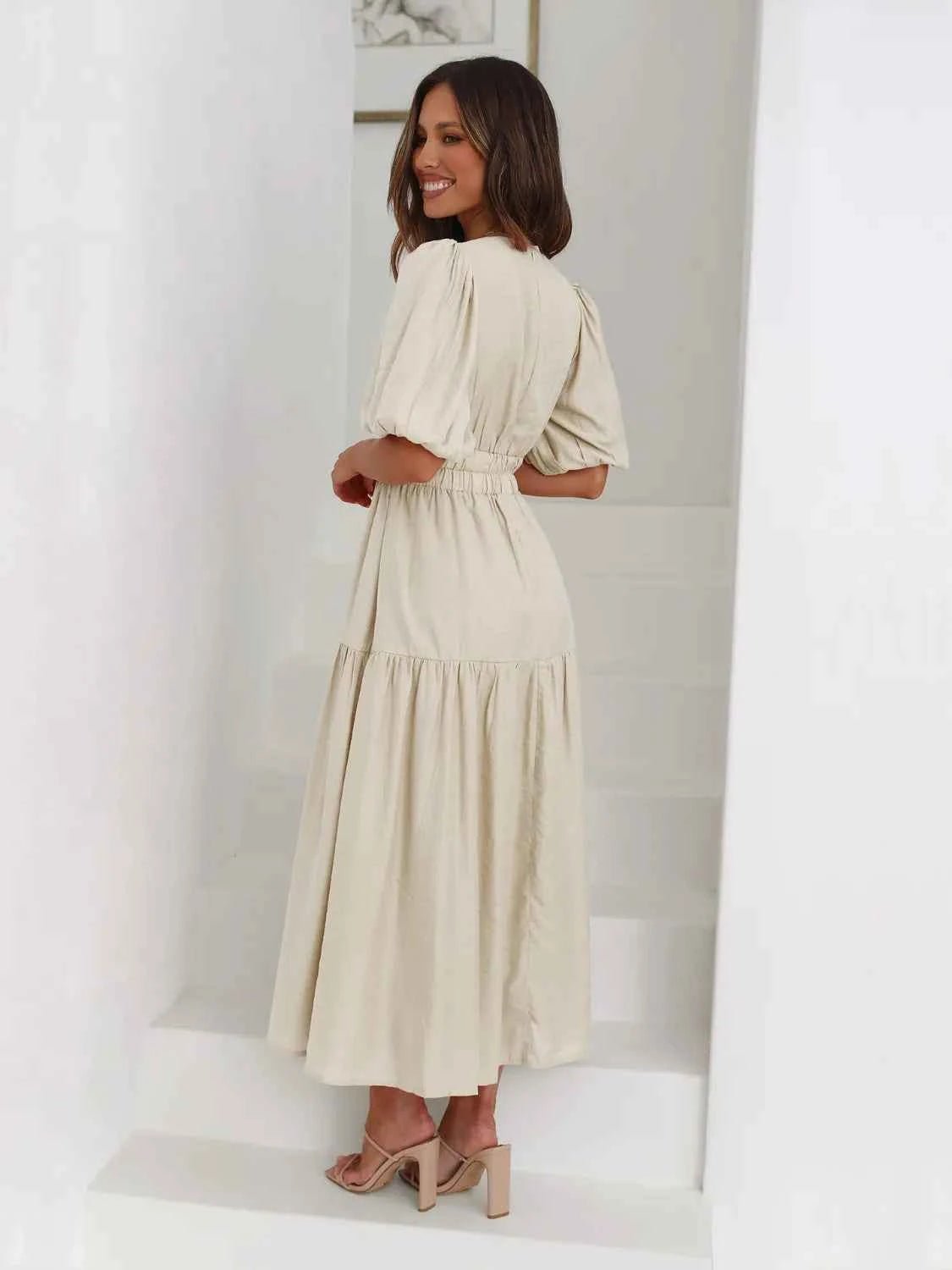 Woman in a beige tiered midi dress with short puff sleeves and a surplice V-neck.