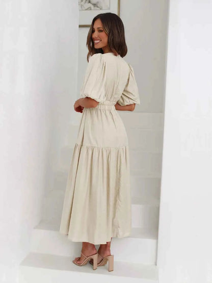 Woman in a beige tiered midi dress with short puff sleeves and a surplice V-neck.
