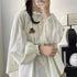 Person wearing a white blouse with ruffled sleeves in a room setting.