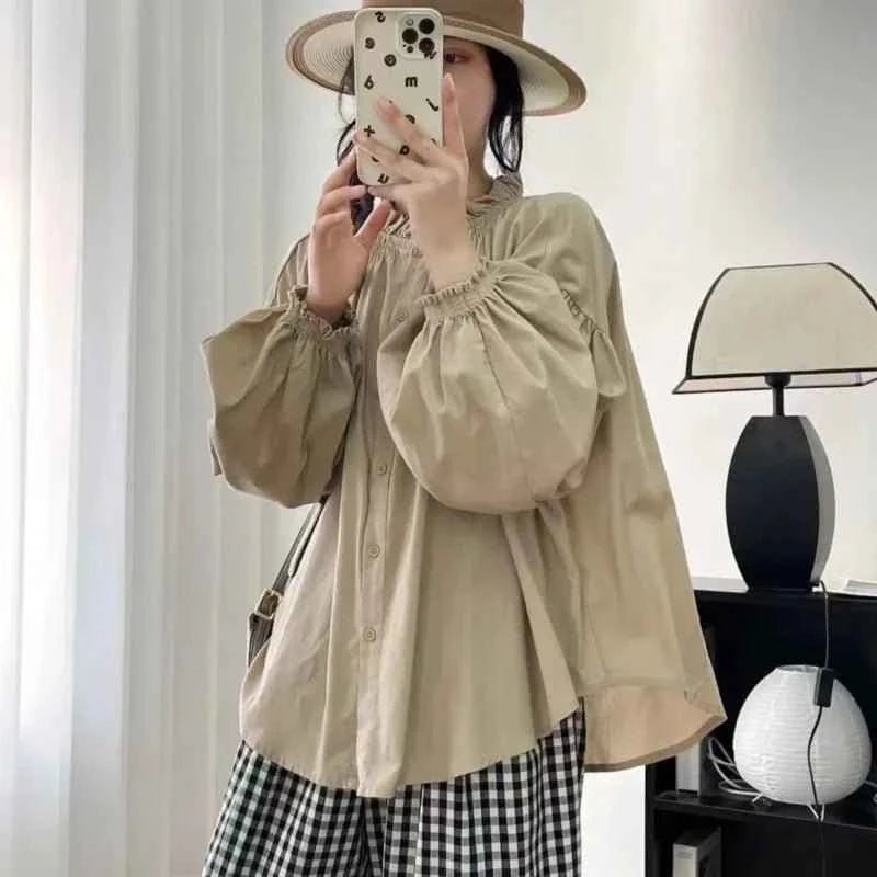 Person wearing a beige blouse and checkered pants taking a mirror selfie.