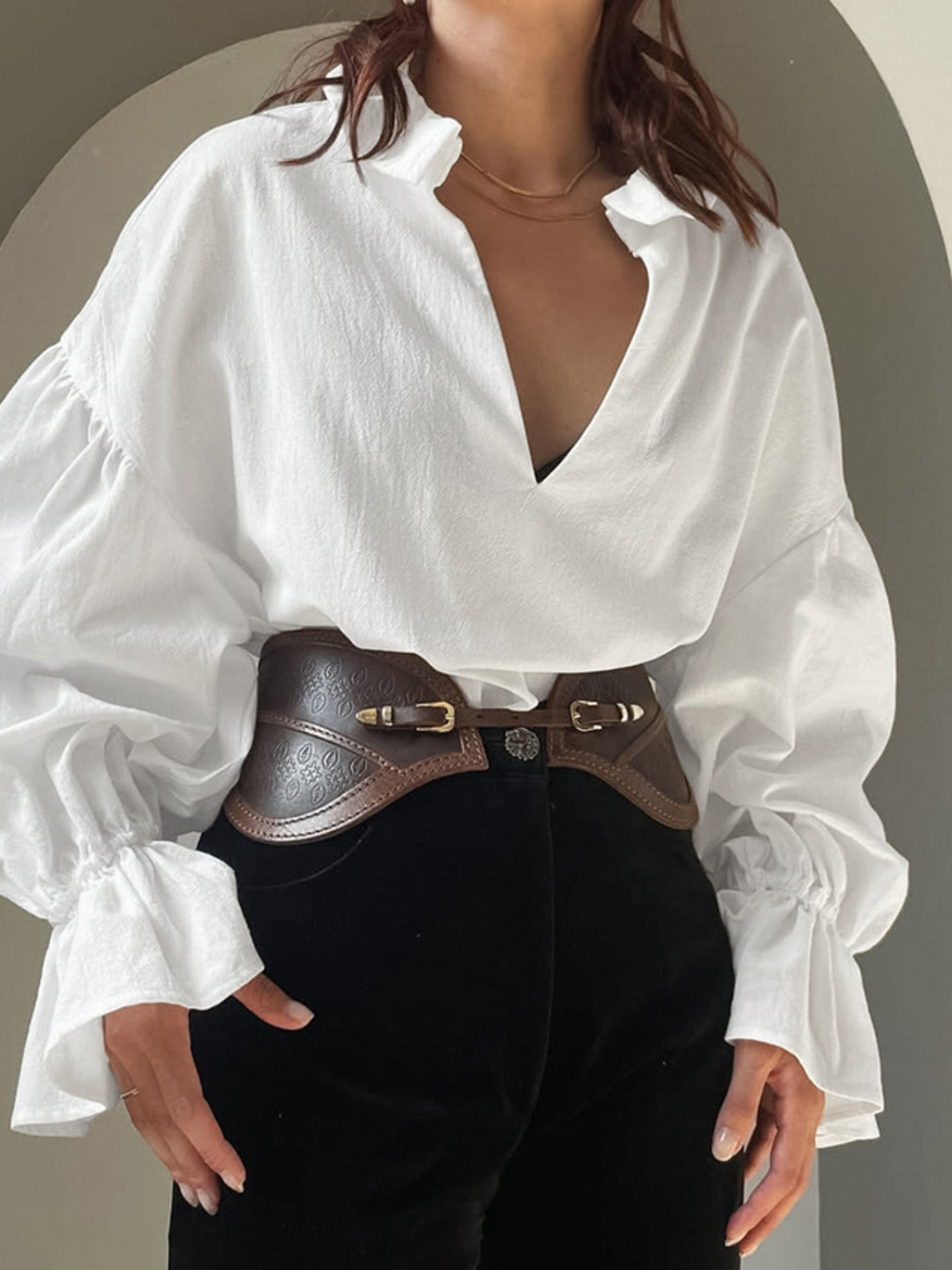 Person wearing a white blouse with a deep neckline and black pants against a neutral background