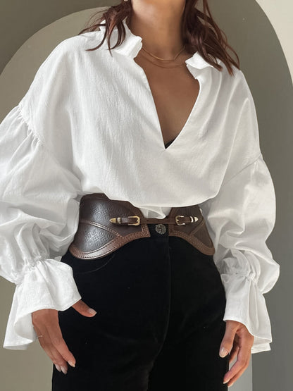 Person wearing a white blouse with a deep neckline and black pants against a neutral background
