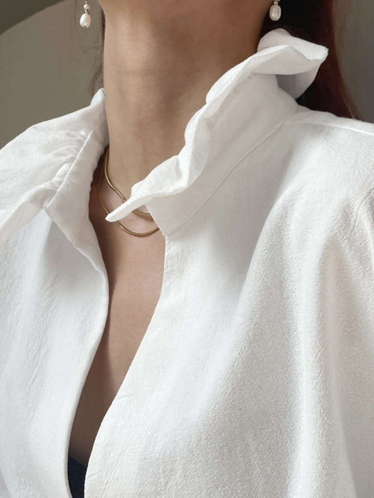 Close-up of a person wearing a white shirt with a ruffled collar, gold necklace, and pearl earrings.
