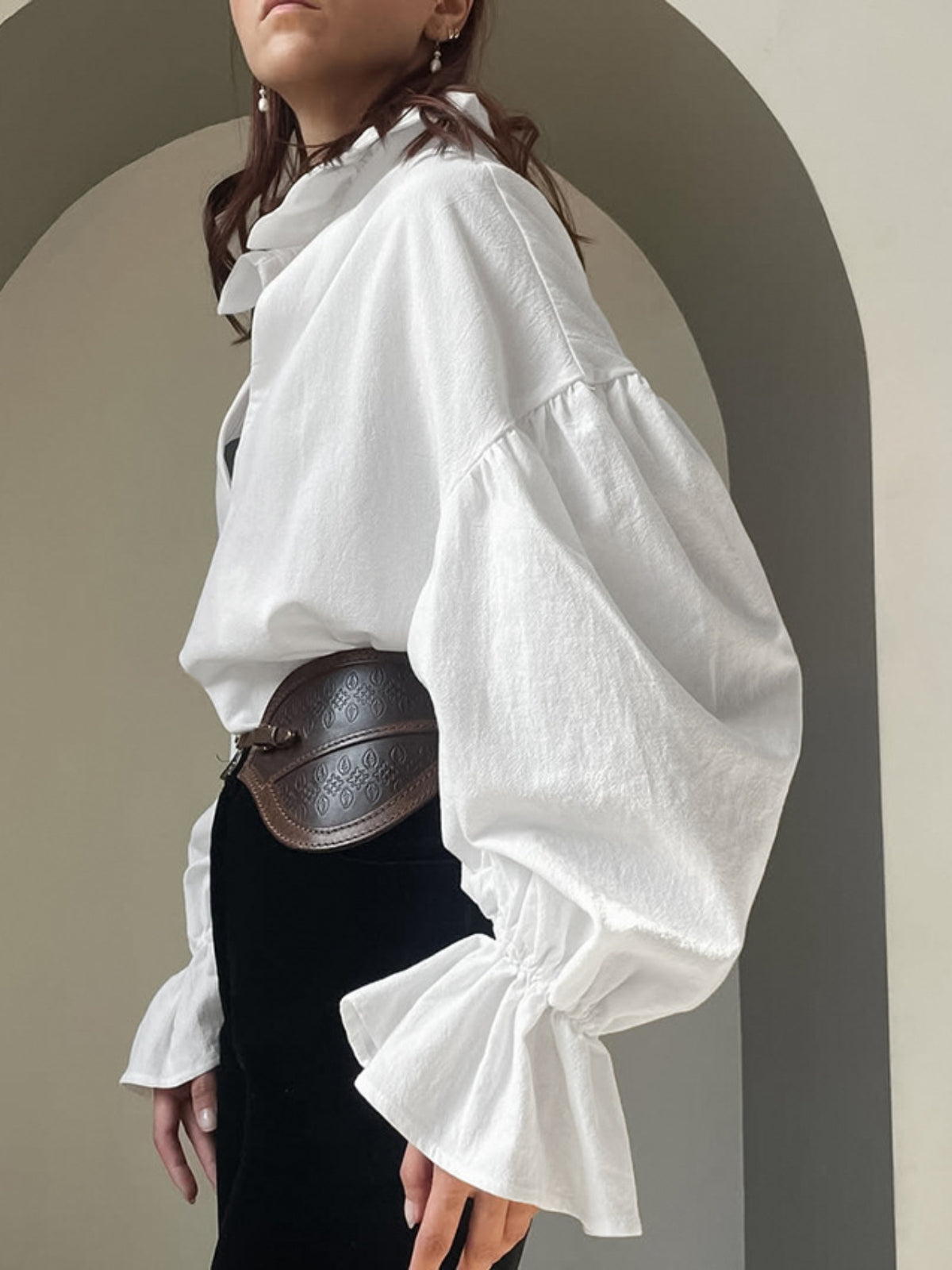 Person wearing a white blouse with puffed sleeves and a black belt against a neutral background