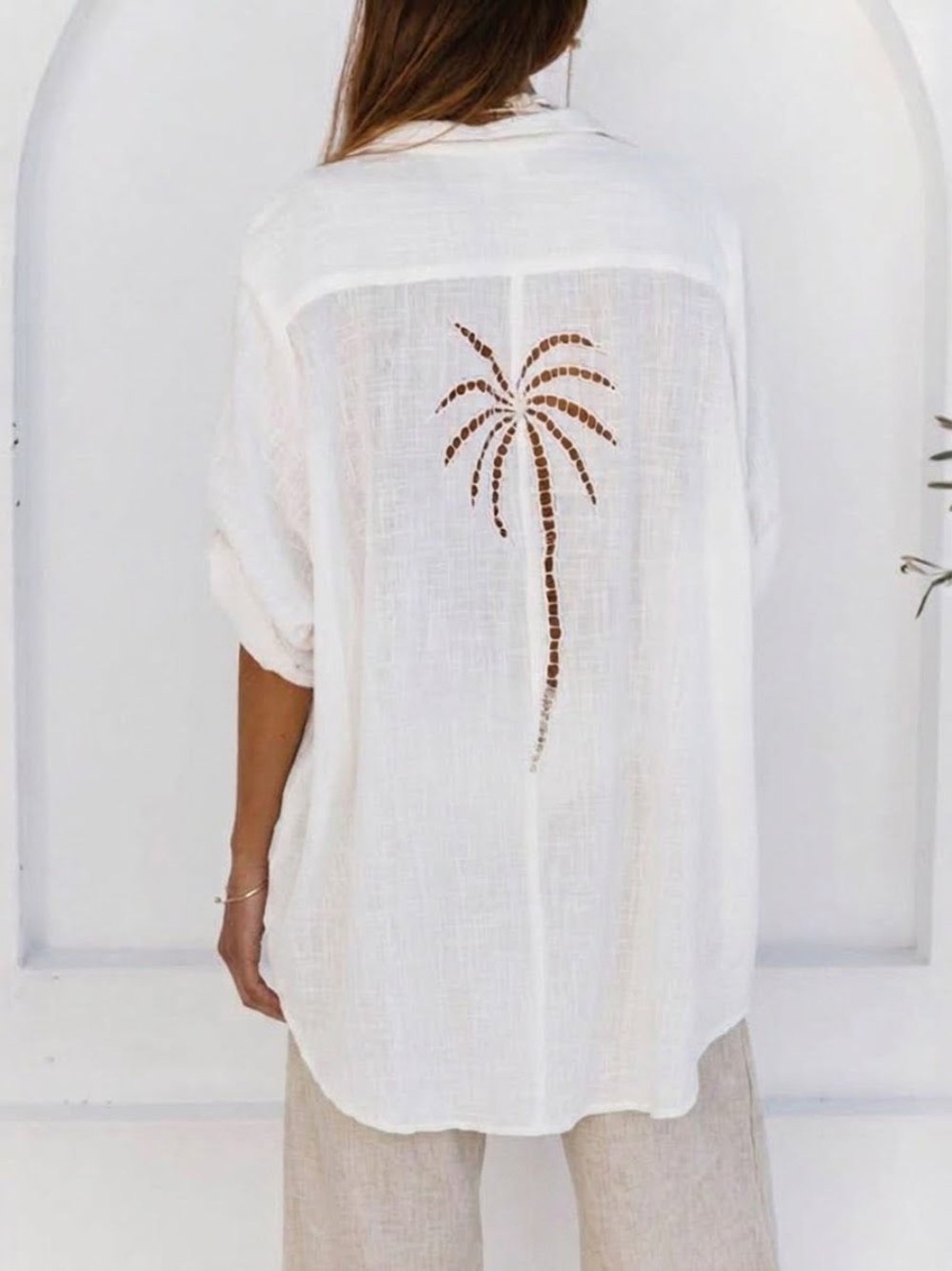 A woman modeling a white linen button-up shirt and matching white linen cropped pants against a light gray studio background.