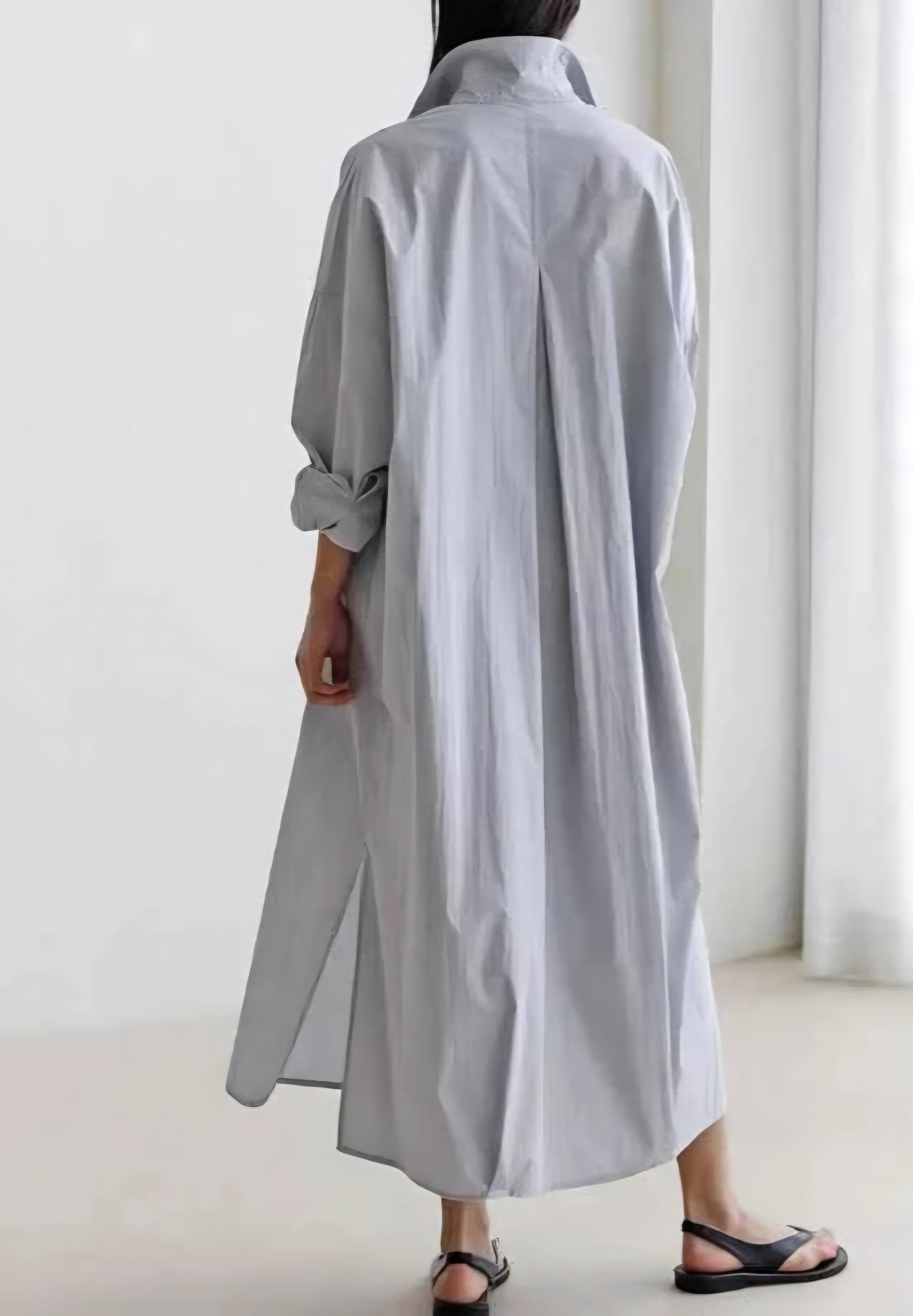 Person wearing a long light gray shirt in a minimalistic setting