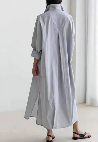 Person wearing a long light gray shirt in a minimalistic setting