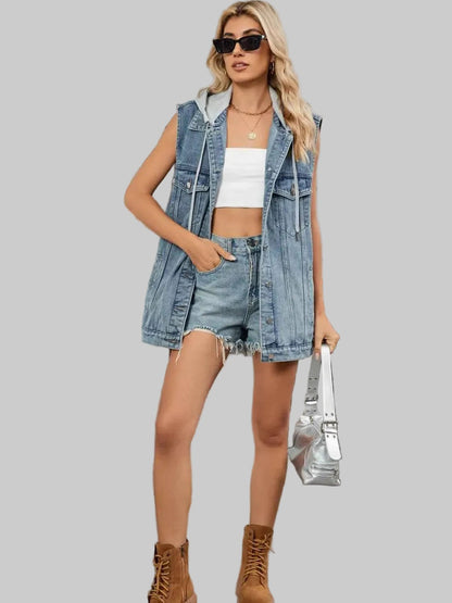 Woman wearing a denim vest, white top, and shorts with brown boots on a gray background