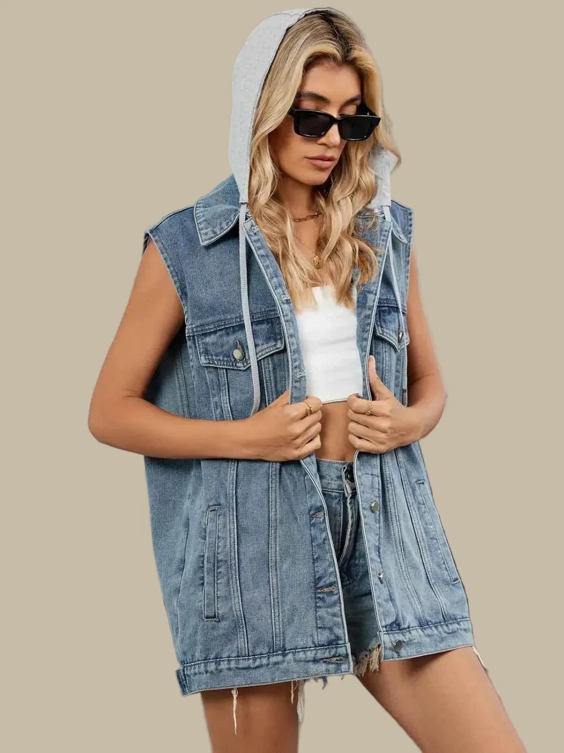 Woman wearing a denim vest over a white top and shorts, standing outdoors.