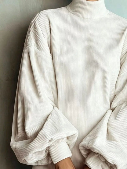 A close-up of a person wearing a ribbed cream-colored mock-neck sweater with voluminous balloon sleeves, set against a neutral gray background.