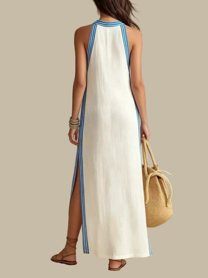 A woman modeling a sleeveless white maxi dress with blue side stripes and a blue-trimmed neckline, holding a woven straw bucket bag against a plain light background.
