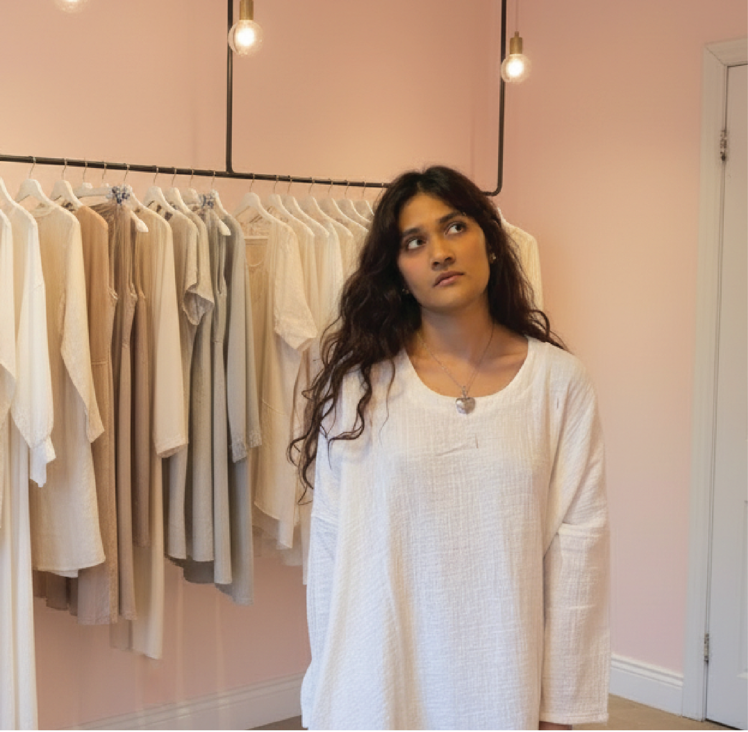 Woman standing in a room with racks of clothes and a mirror on the wall.
