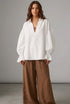 White blouse with ruffled sleeves worn by a person against a neutral background